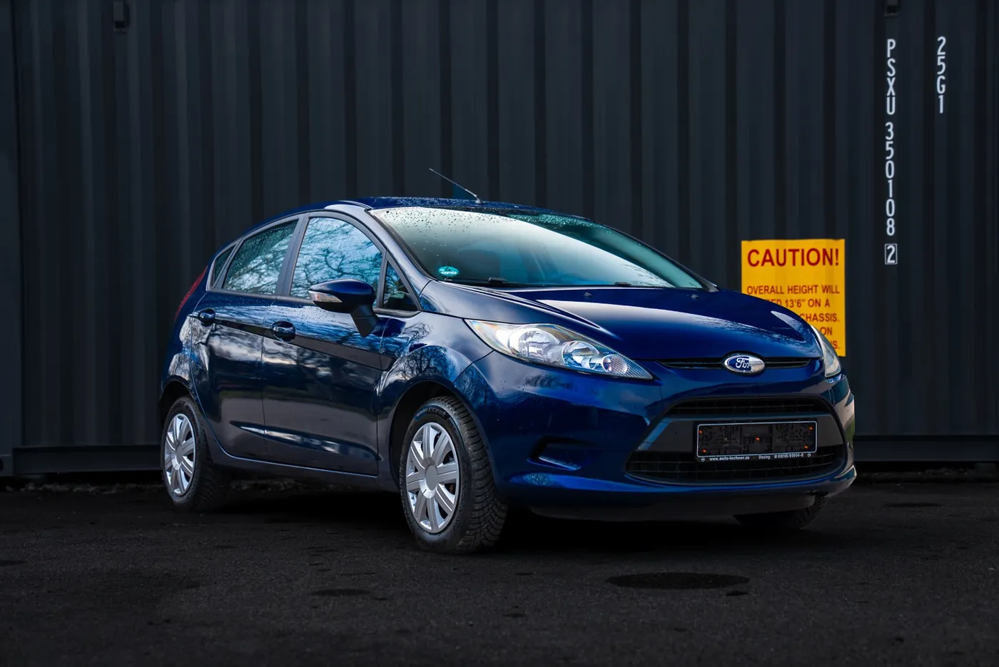 Ford Fiesta in Dunkelblau vor einer schwarzen Containerwand